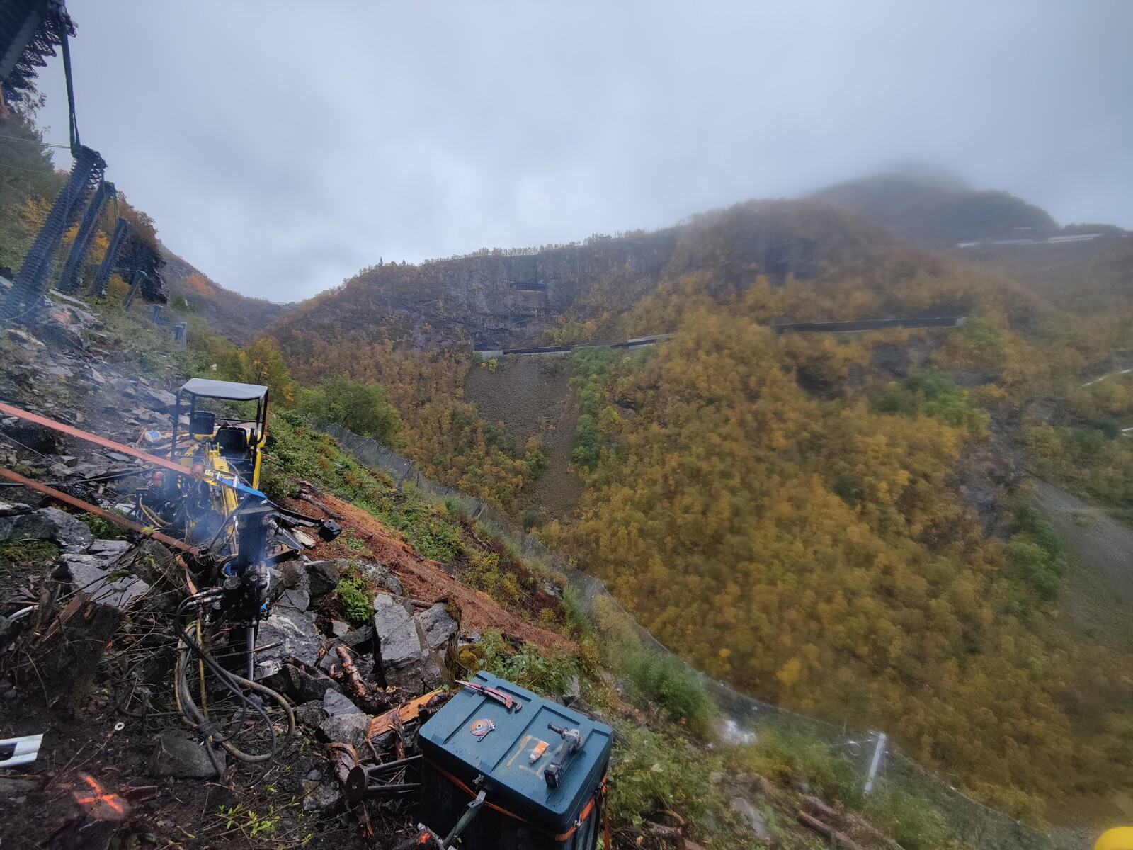 The Menzi Muck drilling a foundation bolt, with Flåmsbana across the valley